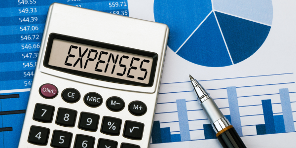 A calculator showing the word 'EXPENSES' on the screen, in the background charts and graphs can be seen