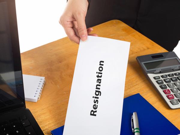 An employee giving a white envelope to their employer with the word 'RESIGNATION' written on the envelope