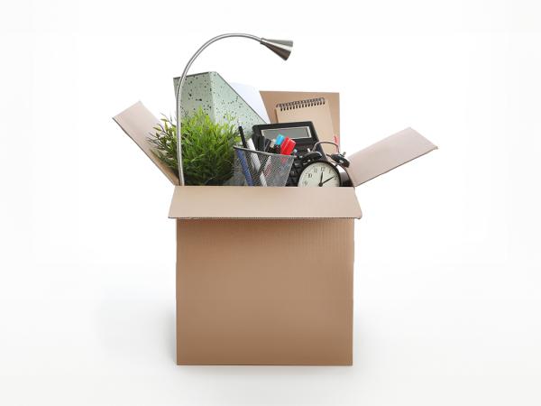 a box packed with office supplies such as a lamp, clock, folders, pen pot and paper pads. 