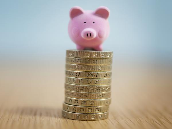 a small pile of old pound coins with a tiny pink pig sat on top. 