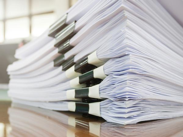 papers grouped into a pack and bound together, many of these packs are stacked in a pile on a desk. 