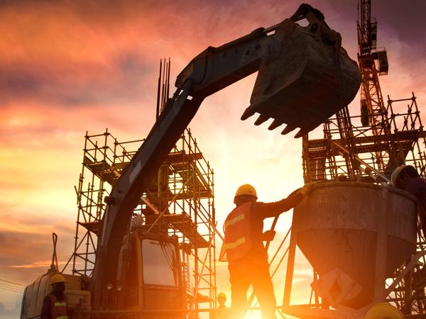 a silhouette of a construction site at sunset showing a digger, some scaffolding, and a couple of workers. 