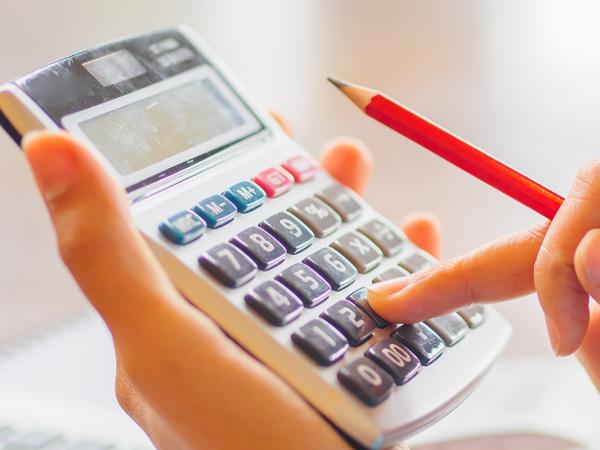 person typing on a calculator whilst holding a pencil