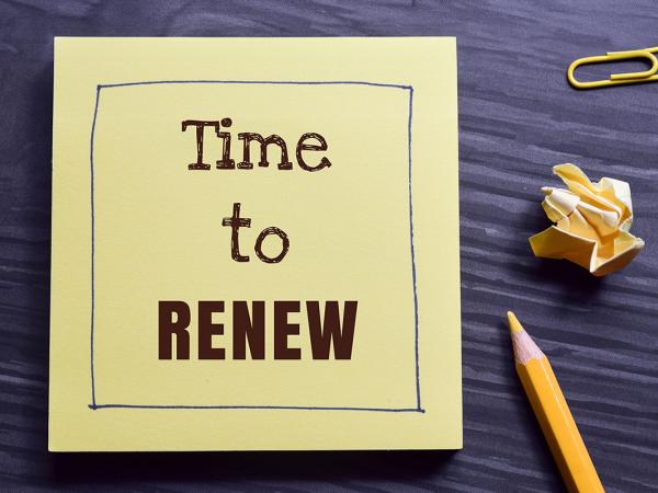 a wooden desk, on top sits a yellow pencil, a yellow paperclip, a screwed up post-it note and a post-it note with the words 'TIME TO RENEW'