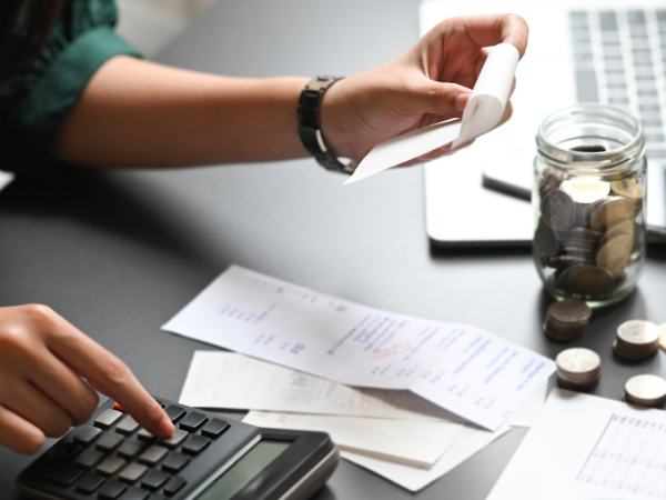 A person sat at a desk, adding up receipts on a calculator. 