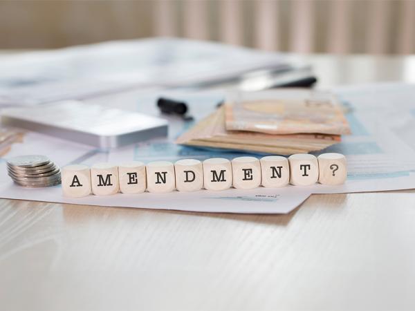 a desk with money and paperwork in the background with wooden blocks spelling out the word 'AMENDMENT'