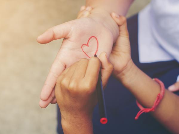 a child drawing a love heart on an adults palm with red pen.