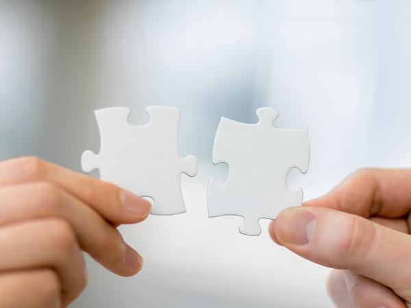 2 people each holding a jigsaw piece, the pieces look as if they fit together 