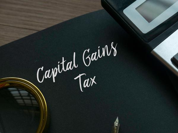 a black book with the words 'CAPITAL GAINS TAX' on the front. next to this is a calculator, a fountain pen and a magnifying glass.