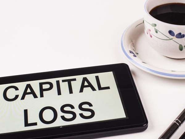 a tablet with the words 'CAPITAL LOSS' typed on the screen, two pens and a cup of black coffee. 