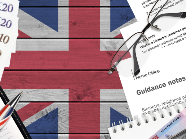 UK flag painted in the background, on top of this various things can be seen, English money, clipboard and pen, USB drive, glasses, residence permit and 'GUIDANCE NOTES' documents