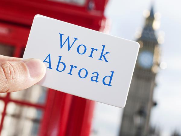 a person holding up a card that says 'WORK ABROAD' in blue text. The background shows the picture was taken in London as Big Ben and a red telephone box can be seen. 