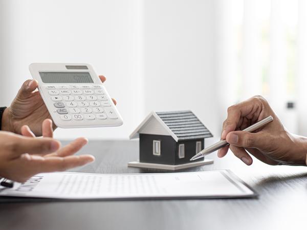 2 people sat at a desk with a contract and a model house in front of them. 