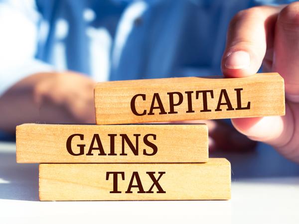 a person stacking wooden blocks, each block has a word written on it spelling out 'CAPITAL GAINS TAX' 