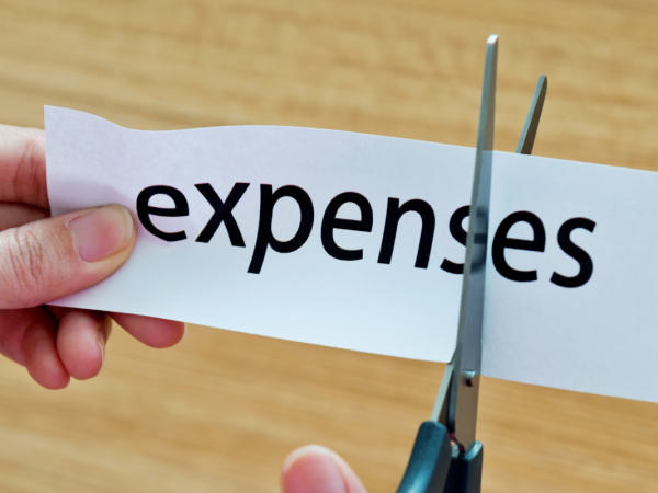 The word "expenses" typed on a piece of white paper, with scissors cutting the letters "e" and "s" at the end of the word.