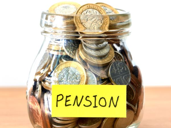 A glass jar filled with coins, a note is stuck to the jar that reads 'PENSION'. 