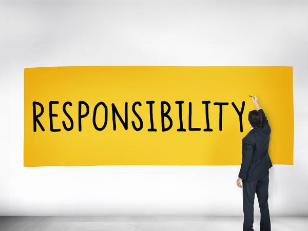 A grey background with a yellow banner, on the banner the word 'RESPONSIBILITY' can be seen being written in black ink by a person standing next to it.