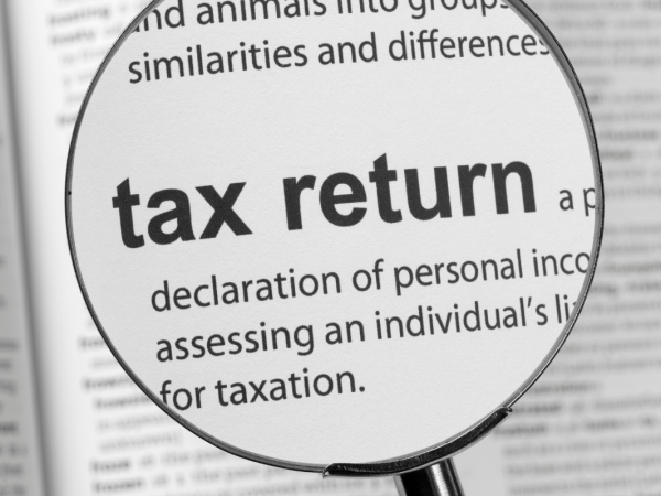 Magnifying glass hovering over the word 'TAX RETURN' in the dictionary. 