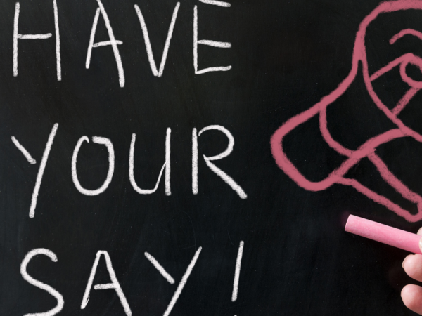 A chalkboard with the words 'HAVE YOUR SAY' in white chalk, next to this a picture of a megaphone is drawn in red chalk.