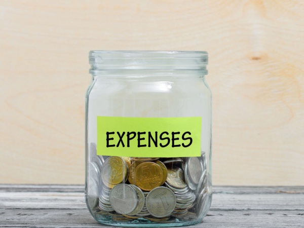 Glass jar with coins inside, the notice on the jar reads 'EXPENSES'.