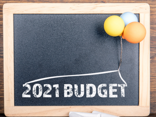 A chalkboard with the words '2021 BUDGET' printed on it, a small bunch o balloons are attached to the chalkboard.