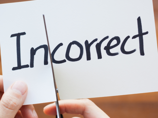 A piece of paper with the word 'INCORRECT' written in black ink, the paper is being cut with scissors in between 'IN' and 'CORRECT' 