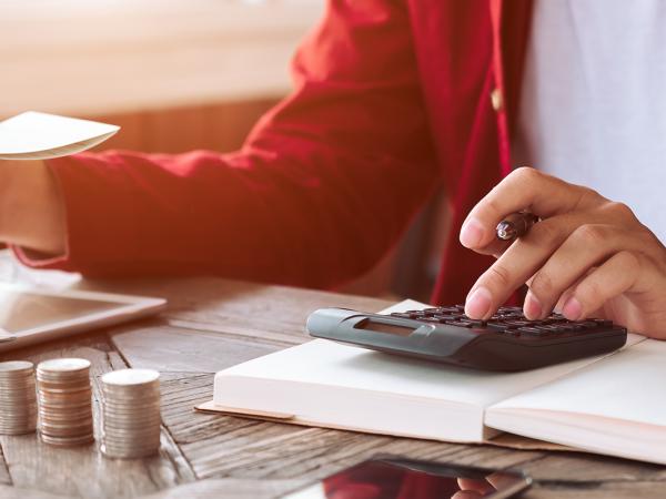 A person sat at a desk with paperwork and a calculator along with stacks of coins.