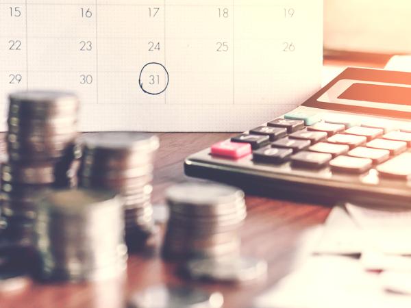 A calendar with a date circled, piles of coins and a calculator.