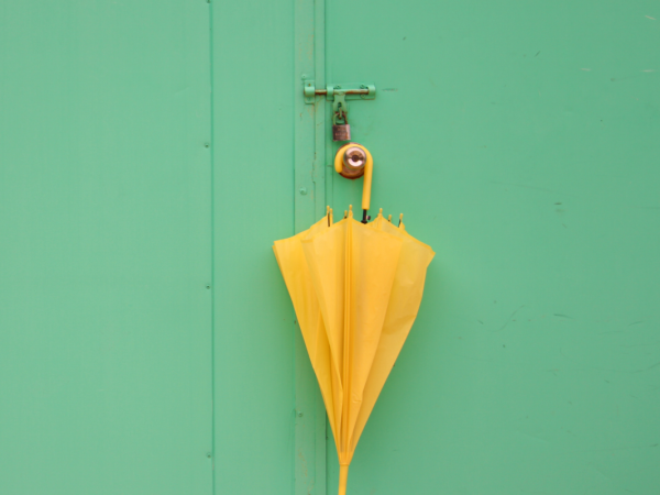 A yellow umbrella hanging on a doorknob against a pale green background. 