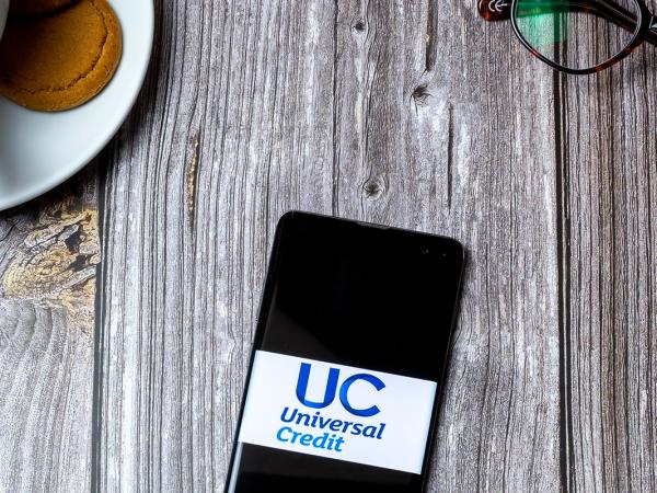 A table with a hot beverage and a mobile phone showing 'UNIVERSAL CREDIT' on the screen.