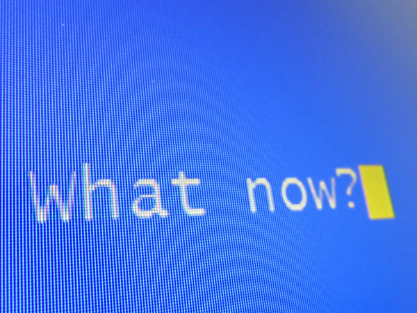A blue computer screen with the words 'WHAT NOW?' typed in white text. 