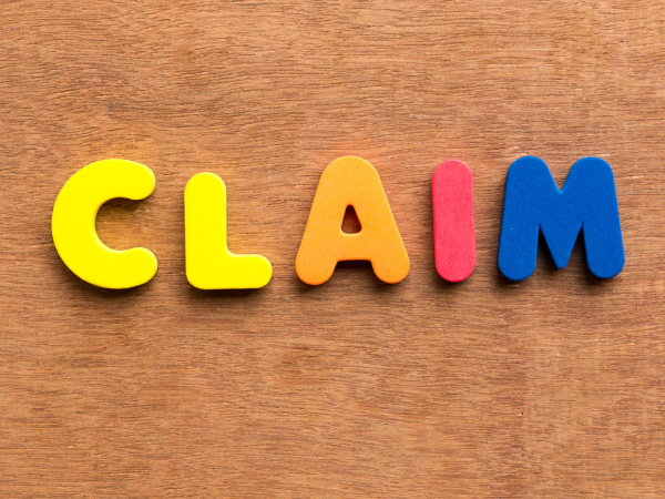 small colourful plastic letters arranged to spell out the word 'CLAIM' against a wooden background. 
