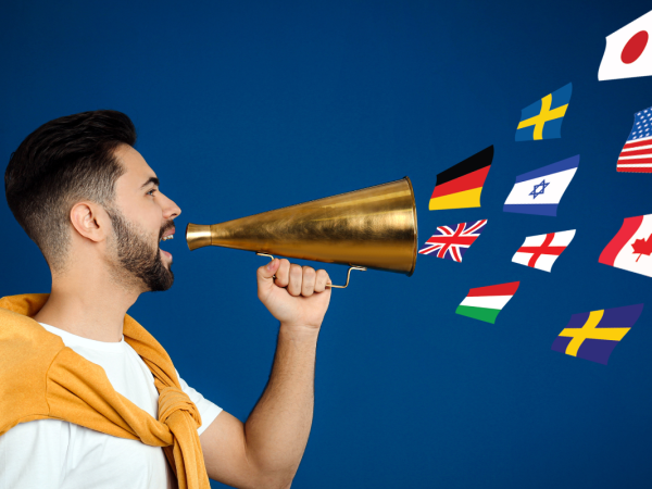 A person holding a cone to their mouth with various international flags floating out of the cone. 
