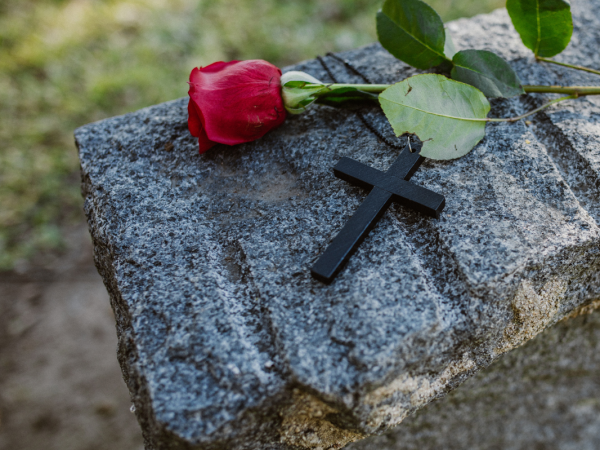 A gravestone with a black cross and a red rose laid on top 