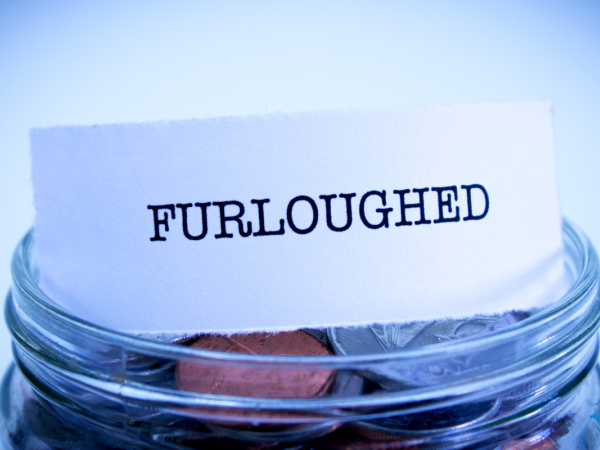 Glass jar of coins with a small piece of paper on top that reads 'FURLOUGHED'