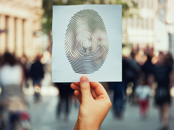 A person holding up an mage of a fingerprint, in the background city streets filled with people can be seen.