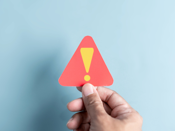 a person holding up a red warning triangle containing an exclamation mark.