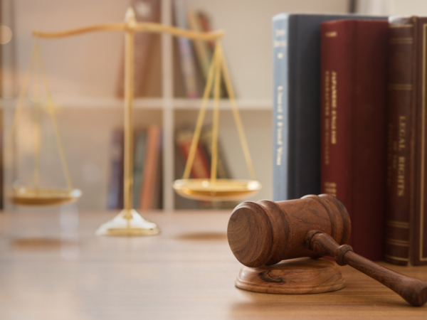 brass scales, a hammer and gavel and legal books can be seen on a desk.