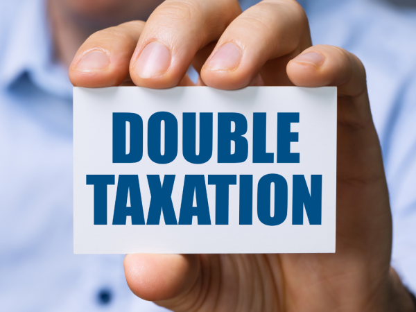 Person holding up a card with the words 'DOUBLE TAXATION' on it in blue text.