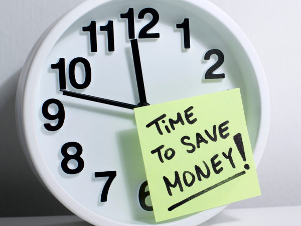 A wall clock with a post it note stuck to the front, the note reads 'TIME TO SAVE MONEY!'