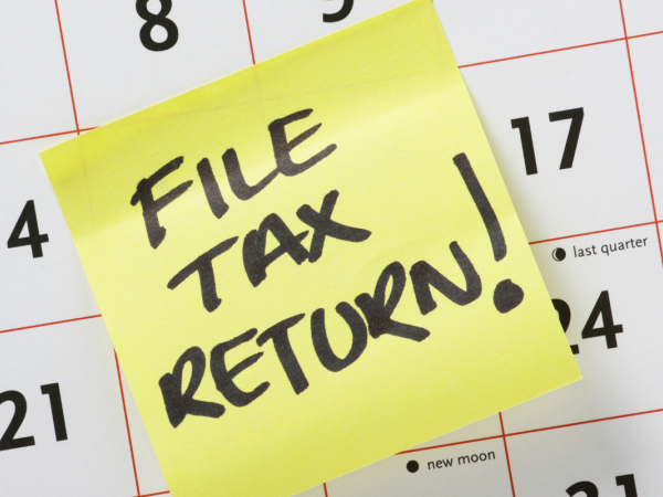 a wall calendar with a yellow post it note stuck to it, the note reads 'FILE TAX RETURN' 
