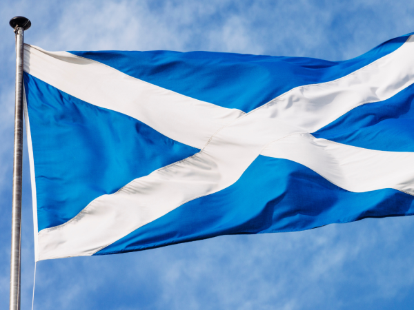 Scottish flag blowing in the wind against a blue sky background.