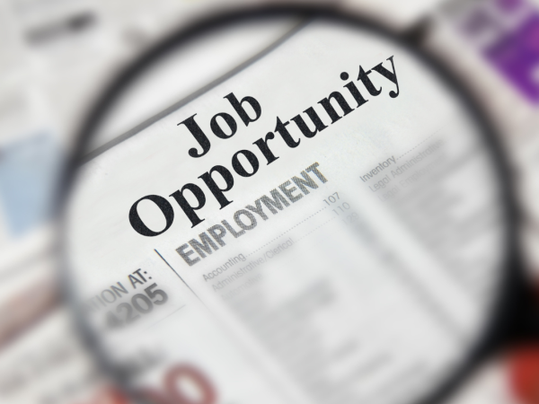 Newspaper showing job listings and a magnifying glass hovering over the words 'JOB OPPORTUNITY'