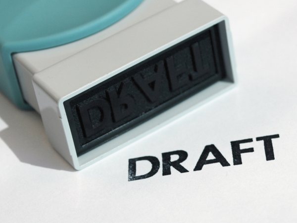 A hand stamper and the word 'DRAFT' stamped onto a white surface