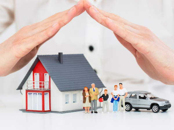 A person's hands covering a model home, car and tiny family to protect them.