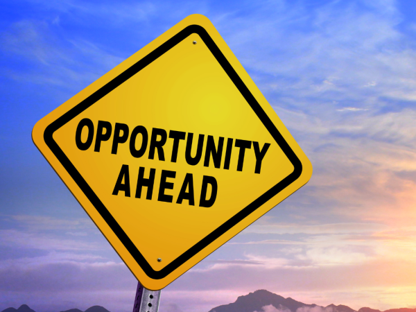 A yellow road sign with the words 'OPPORTUNITY AHEAD' in black text, a sunset can be seen in the background