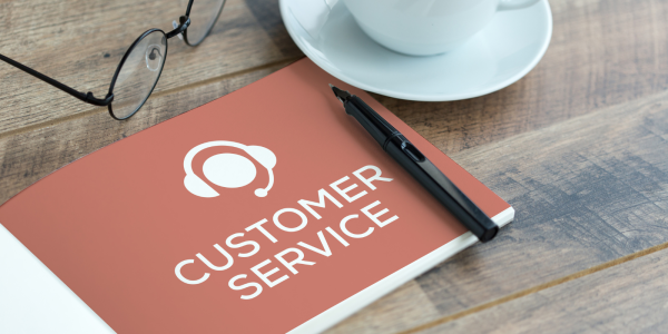 a booklet titled 'CUSTOMER SERVICE' on a desk besides a pair of glasses and a cup of tea.