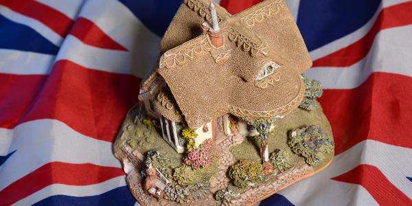 background is the UK flag, on top of this is a model of a traditional English cottage