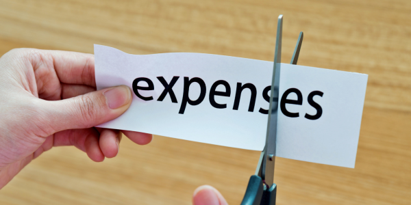 The word "expenses" typed on a piece of white paper, with scissors cutting the letters "e" and "s" at the end of the word.