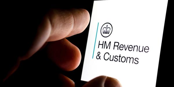 A person looking at their smartphone, the screen shows the HMRC logo. 'HM REVENUE & CUSTOMS'. 